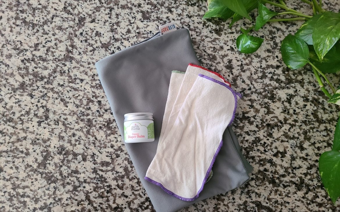 Image of gray wet bag, a diaper cream container, and three cloth wipes on top of a granite countertop.