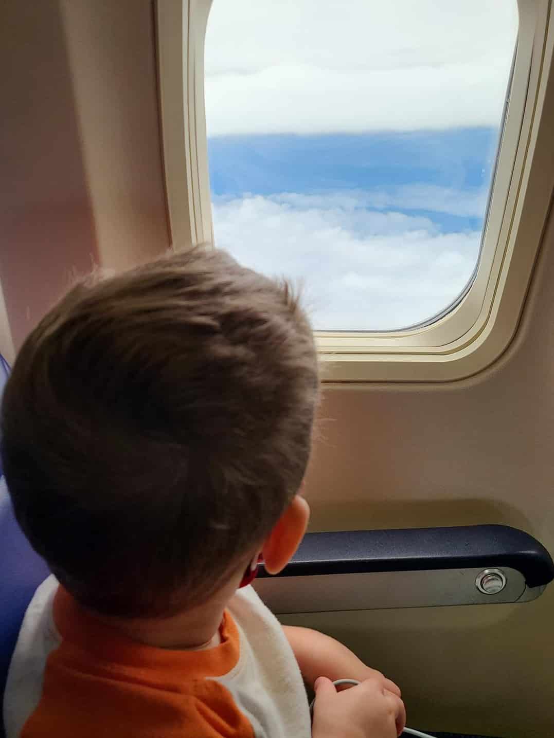 Kid looking out the window of an airplane - flying on a biofueled airplane as an eco-friendly travel tips for families