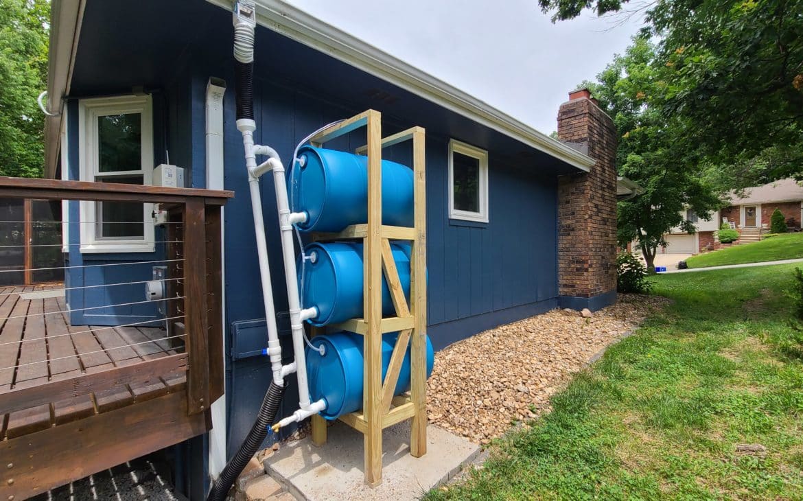 DIY stacked rain barrel system completely assembled beside blue house