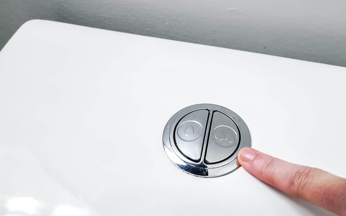 DIY sustainably by including efficient dual flush toilets. Finger is pointing to a dual flush toilet button.