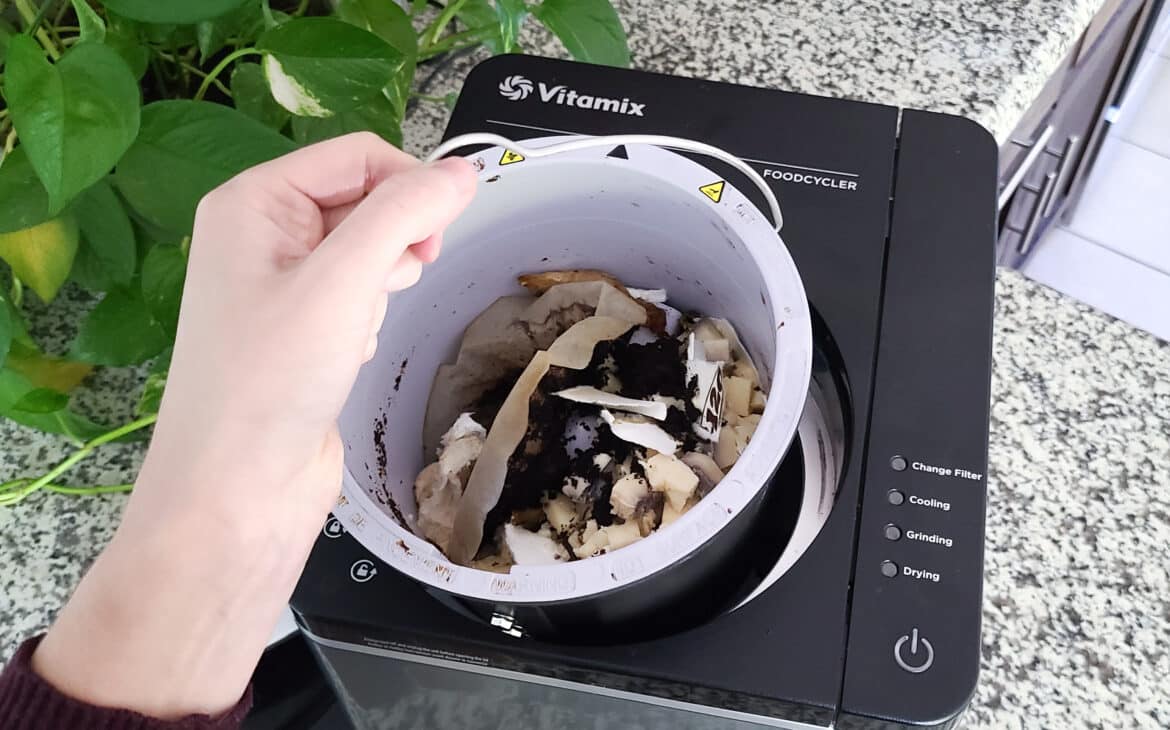 Hand placing the removable bucket of the Vitamix Foodcycler into the base electric composter appliance