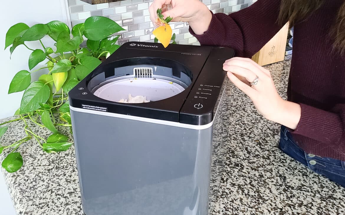Gift for sustainability lovers -  showing electric composter on a countertop with woman placing food scraps in it.
