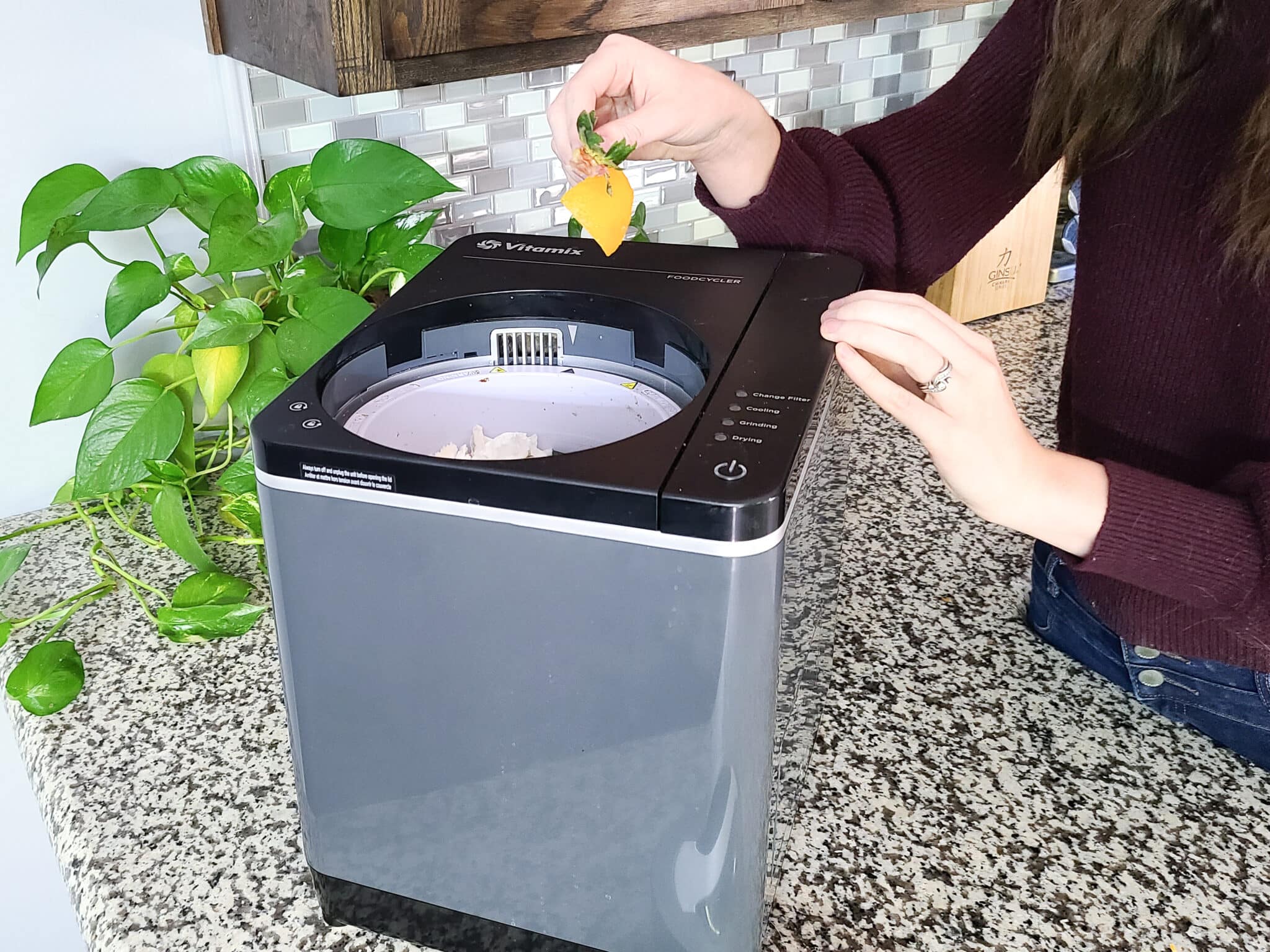 Woman putting orange peel and strawberry food scraps into the Vitamix Foodcycler electric composter