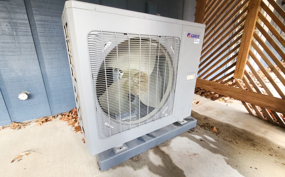 Heat pump vs. furnace - showing a heat pump compressor sitting outside a blue house on concrete